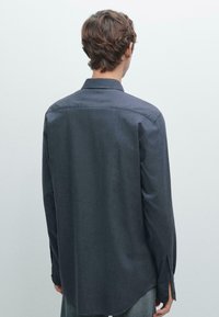 Dark blue long-sleeve shirt made of a textured fabric, featuring a standard collar, buttoned cuffs, and a curved hemline.