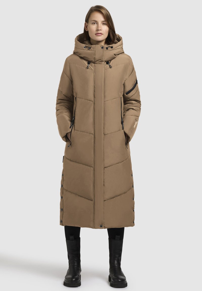 Garš brūns pūkains mētelis ar kapuci, kas izceļas ar strukturētu dizainu, priekšējo rāvējslēdzēju, sānu kabatām un pogu akcentiem apakšmalā.