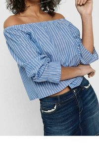 Blusa azzurro chiaro off-the-shoulder con strisce verticali bianche, maniche lunghe a sbuffo e orlo corto, abbinata a jeans scuri strappati.