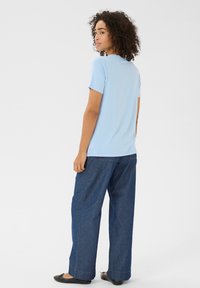 T-shirt bleu à manches courtes en tissu doux, associé à un pantalon en denim foncé amplement coupé et des chaussures plates noires, présenté sous un angle arrière.