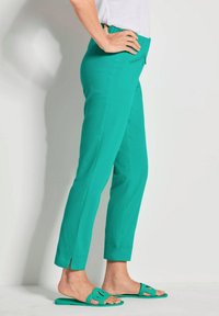 Pantalons cropped turquoise avec un léger éclat, dotés d'une poche zippée et d'une fente à l'ourlet. Associés à des sandales à glissière vertes assorties.
