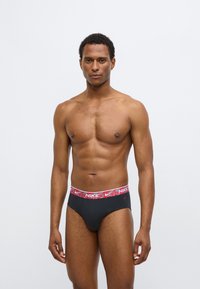 Pánské černé slipy s červenobílým vzorovaným pasem s logem Nike. Hladká tkanina a těsný střih pro pohodlí a oporu.