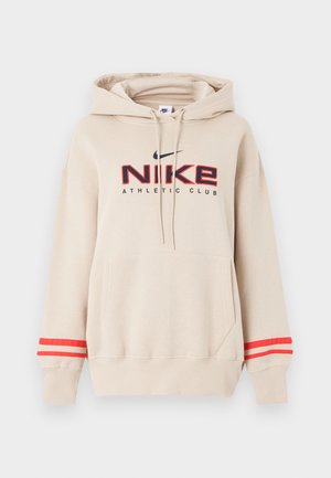 Beige Nike-hettegenser med frontlomme, røde striper på ermene, og "Nike Athletic Club"-logo i svart og rødt på brystet.