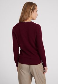 Bordeauxroter Strickpullover mit langen Ärmeln und geripptem Saum. Hat einen runden Halsausschnitt und eine taillierte Silhouette. Glatte Textur.