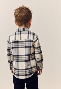 Kariertes Flanellhemd zum Zumknöpfen in Weiß, Blau und Beige. Mit Kragen, langen Ärmeln und abgerundetem Saum. Rückwärts getragen.