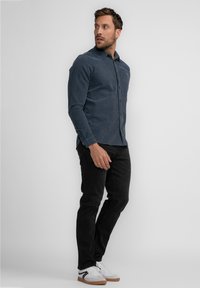 Donkerblauwe lange mouw shirt van een zachte stof, met een button-down kraag en bruine knopen, gecombineerd met zwarte jeans en witte sneakers.