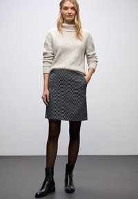 Ljusgrå stickad tröja med hög krage, i kombination med en svartvit zigzag-mönstrad kjol. Svarta ankelstövlar fulländar looken.