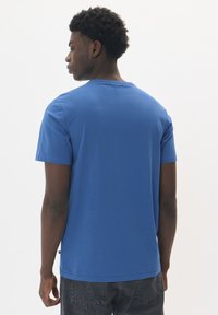 Camiseta de algodón azul con cuello redondo, mangas cortas y dobladillo recto. Textura suave, diseño simple y sin patrones ni logotipos prominentes.