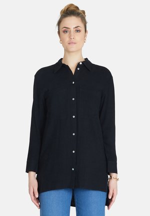 Black button-up shirt with a collar, two chest pockets, long sleeves, and a hem that extends past the hips; made of textured fabric.
