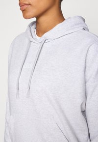Hoodie cinza feito de um tecido macio, com capuz ajustável, bolso frontal e um pequeno logótipo branco no peito.