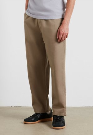 Pantaloni beige a vestibilità ampia realizzati in tessuto misto cotone, dotati di tasche laterali, gambe dritte, abbinati a sneakers nere.