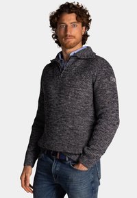 Marineblauw en grijs gebreid sweater met een hoge kraag en een halve rits; voorzien van ribbelstructuur en een logo-oppatch op de linkerschouder.