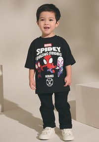 Černé tričko s grafikou Spidermana, v kombinaci s černými kalhotami a bílými teniskami. Jednoduchý střih, krátké rukávy a barevné potisky.