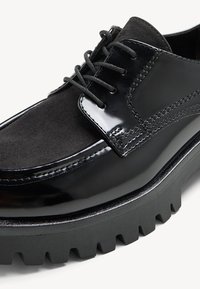Schwarze Lederschuhe mit glänzender Lackoberfläche und Wildlederakzenten. Mit einer klobigen, strukturierten Sohle und traditionellem Schnürdesign.