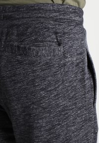 Dark gray, textured joggers featuring a back pocket and an elastic waistband. Fabric has a subtle heathered pattern with a soft finish.