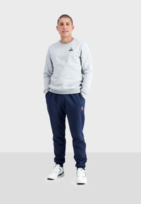Sudadera gris con logo, pantalones jogger azul marino y zapatillas blancas. Diseño elegante, tejido suave, detalles en los puños y la cinturilla con canalé.