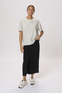 T-shirt gris clair à manches courtes et légèrement texturé, associé à une jupe midi noire avec une fente devant, et des baskets blanches.