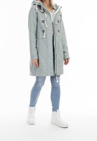 Světle modrý kabát s kapucí na celou délku se zipem, detaily s přezkami a strukturovanou látkou. Kombinováno se světlými džínami a bílými vysokými teniskami.