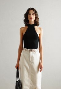 Black halter top, fitted design, cream denim skirt, floral belt, black handbag, plain background, model with wavy hair.