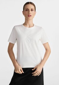 Biała bawełniana koszulka z krótkim rękawem, ozdobiona wyszywaną sylwetką ptaka w tonacji na przodzie. Miękka tekstura, okrągły dekolt.