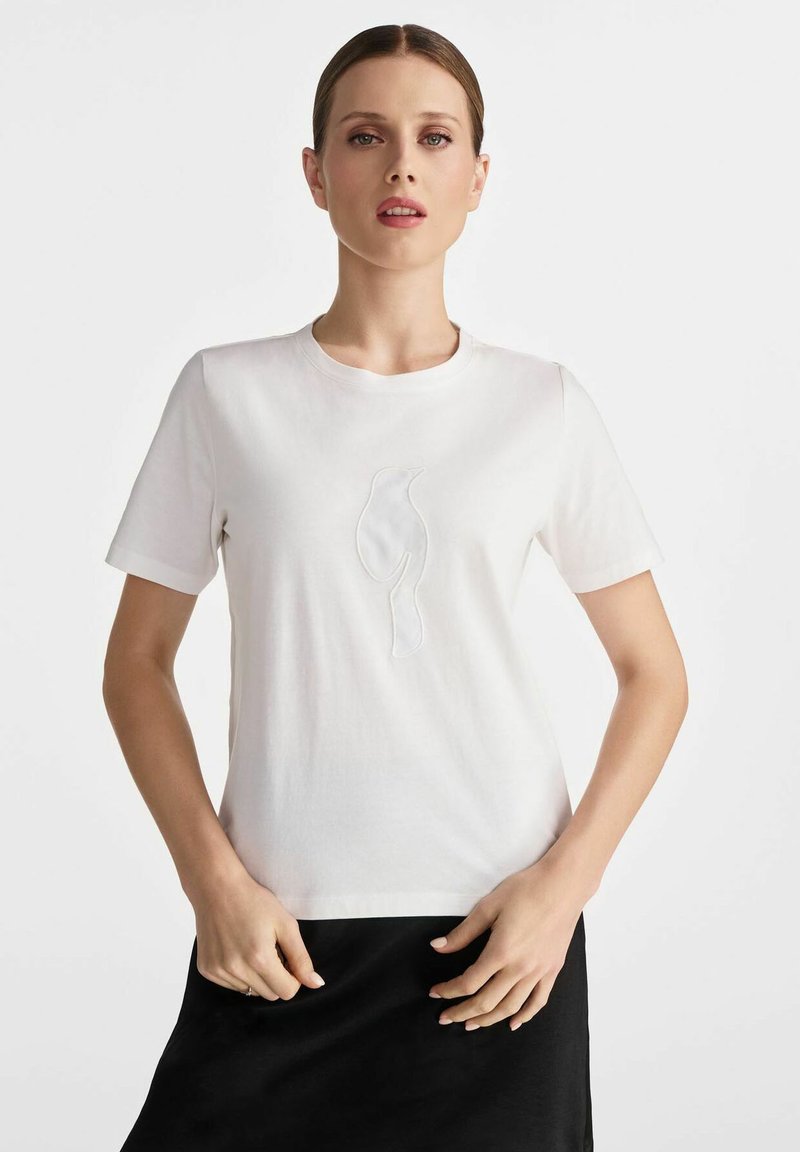 Biała bawełniana koszulka z krótkim rękawem, ozdobiona wyszywaną sylwetką ptaka w tonacji na przodzie. Miękka tekstura, okrągły dekolt.