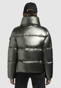 Pufferjack in metallic donkergroen met een hoge kraag, horizontale quiltpatronen en elastische manchetten. Bevat een klein logo aan de zijkant.