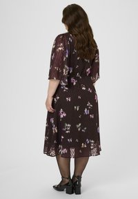 Virágmintás ruha sötét háttérrel, rövid ujjakkal, kiemelt derékkal és lebegő szegéllyel. Fekete bokapántos cipők egészítik ki a megjelenést.