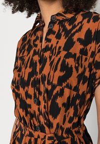 Abito camicia in stampa animale arancione e nera, dotato di colletto, chiusura con bottoni e due tasche sul petto. Tessuto morbido con vita cintata.