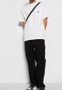Biała bawełniana koszulka z czarnym paskiem na ramieniu, z kieszenią na piersi z prostokątnym logo. W zestawie z czarnymi spodniami i sneakersami.