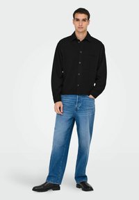 Black button-up shirt with a chest pocket, paired with loose-fitting light blue jeans and black footwear. Clean, minimalistic design.