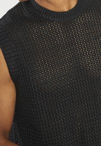 Top de punto negro sin mangas con un patrón de tejido abierto y texturizado, y un cuello redondo acanalado, que resalta su diseño aireado y material.
