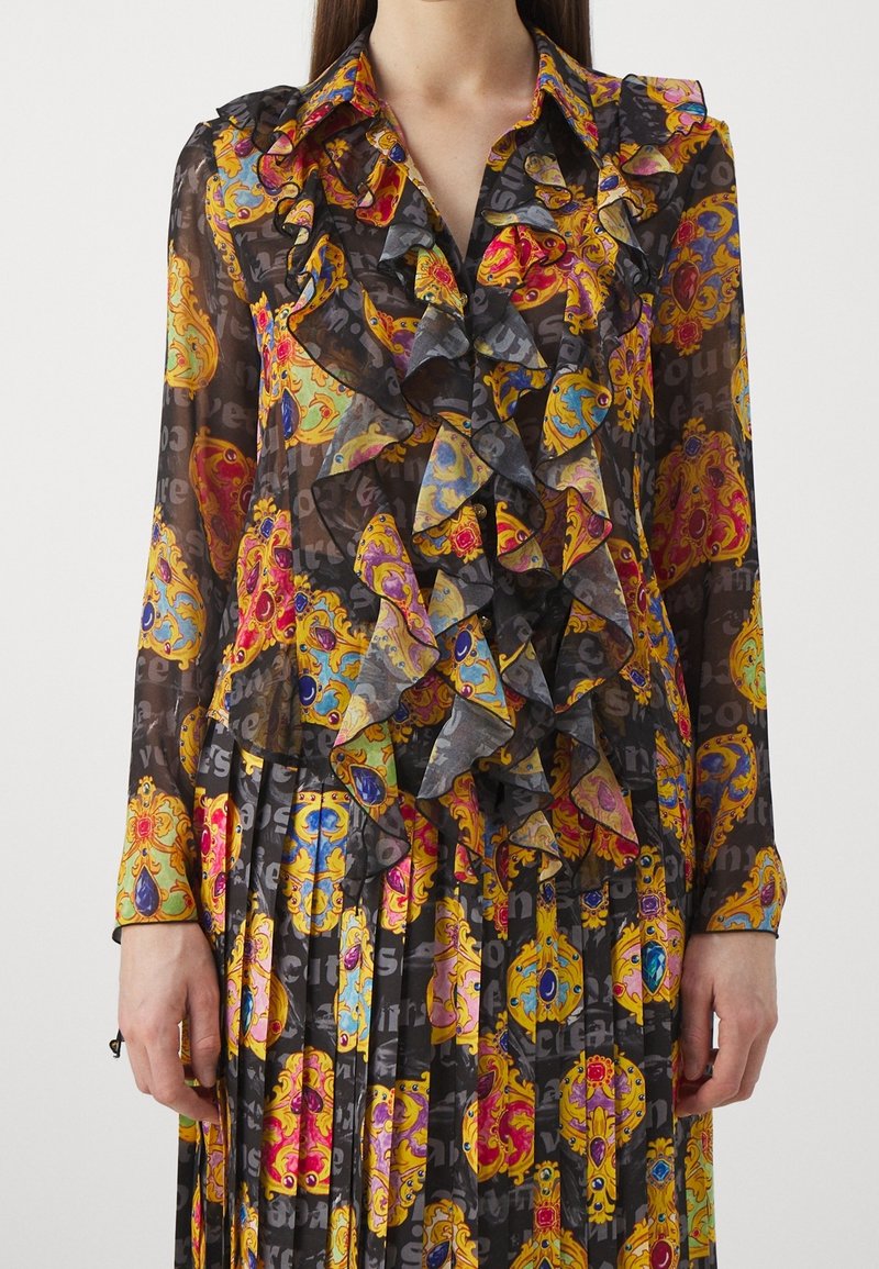 Ensemble blouse noire transparente et jupe plissée avec des motifs baroques colorés et ornés, et des volants superposés à l'avant.