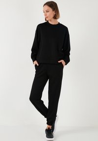 Completo sportivo nero composto da una felpa a girocollo con maniche lunghe e pantaloni joggers abbinati con polsini elasticizzati. Indossato con sneakers nere.