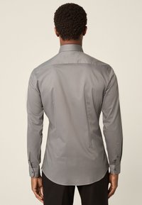 Szürke hosszú ujjú ing sima textúrával, strukturált gallérral és hátsó betéttel. Gombos mandzsettákkal és ívelt aljjal rendelkezik.