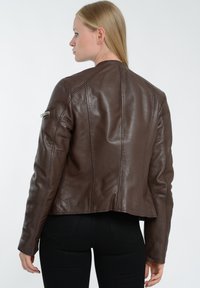 Brun læderkort jakke med strukturerede syninger og lynlås-lommer på ærmet. Glat tekstur, tætsiddende design.