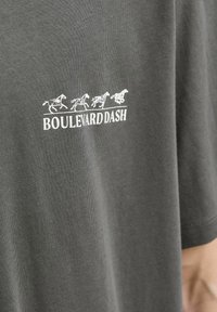 Sivi pamučni majica sa bijelim grafičkim prikazom konja u galopu iznad teksta "BOULEVARD DASH", s opuštenim krojem i kratkim rukavima.