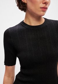 Juodas raukšlėtas mezginys su trumpomis rankovėmis, apvaliu iškirpimu ir subtiliu blizgesiu. Lygus audinys, prigludęs dizainas.