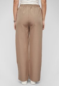 Lichtbruine wijde broek met een elastische tailleband, gemaakt van een gestructureerde stof, gecombineerd met witte sneakers. Eenvoudig en recht gesneden ontwerp.