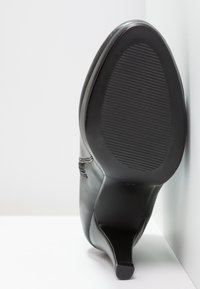 Černá kožená vysoká podpatková bota s špičatou špičkou a texturovanou gumovou podrážkou s horizontálními drážkami pro lepší přilnavost.