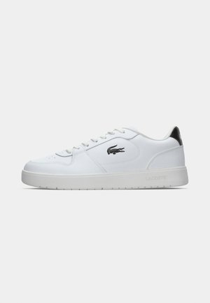 White sneakers made of synthetic material with a smooth texture, featuring a lace-up design, black accent at the heel, and Lacoste logo.