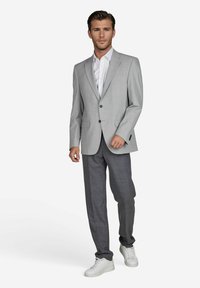 Hellgrauer Blazer mit Reverskragen und Zwei-Knopf-Verschluss, kombiniert mit dunkel gemusterten Hosen und weißen Sneakers. Glatte Stoffstruktur.