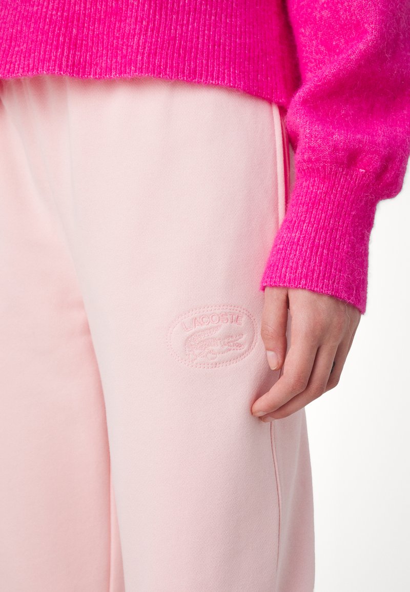 Pull en rose fait de matière tricotée texturée, associé à un pantalon de survêtement rose clair avec un logo embossé sur la cuisse.