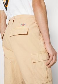 Beige cargobyxor med sidofickor och en bakficka med lock. Tillverkade av mjukt tyg med en subtil struktur och en broderad logodetalj.