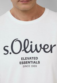 Biała bawełniana koszulka z okrągłym dekoltem, z czarnym nadrukiem: "s.Oliver ELEVATED ESSENTIALS SINCE 1969" w wyraźnej, nowoczesnej czcionce.