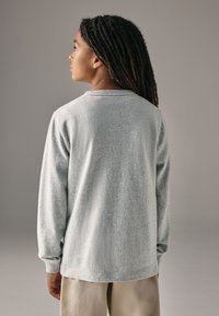 Grijze sweater met lange mouwen van een gestructureerde stof, geribde halslijn en manchetten, gezien van achteren, gecombineerd met beige broek.