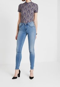 Blå skinny jeans med høj talje, der har en glat tekstur og en tætsiddende silhuet, parret med en mønsteret t-shirt med korte ærmer.