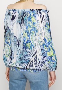Off-shoulder top i let stof med blå, grønne og hvide abstrakte mønstre. Elastisk halsudskæring og rynket kantdetalje.