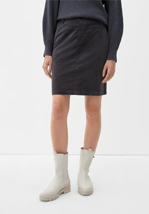 Jupe noire, de longueur genou, en tissu texturé avec une silhouette ajustée. Associée à des bottes en caoutchouc beige clair, mi-mollet, avec une semelle épaisse.