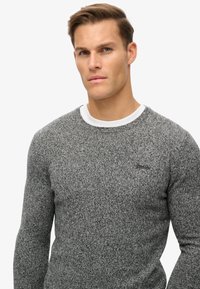 Szary, teksturowany sweter dzianinowy z okrągłym dekoltem. Posiada warstwowy biały kołnierz oraz subtelną markę na klatce piersiowej. Slim fit.