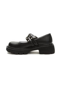 Zapatos Mary Jane de cuero negro con suela de goma gruesa, correa ajustable con tachuelas plateadas y diseño de punta redonda. Detalle de costuras reforzadas.